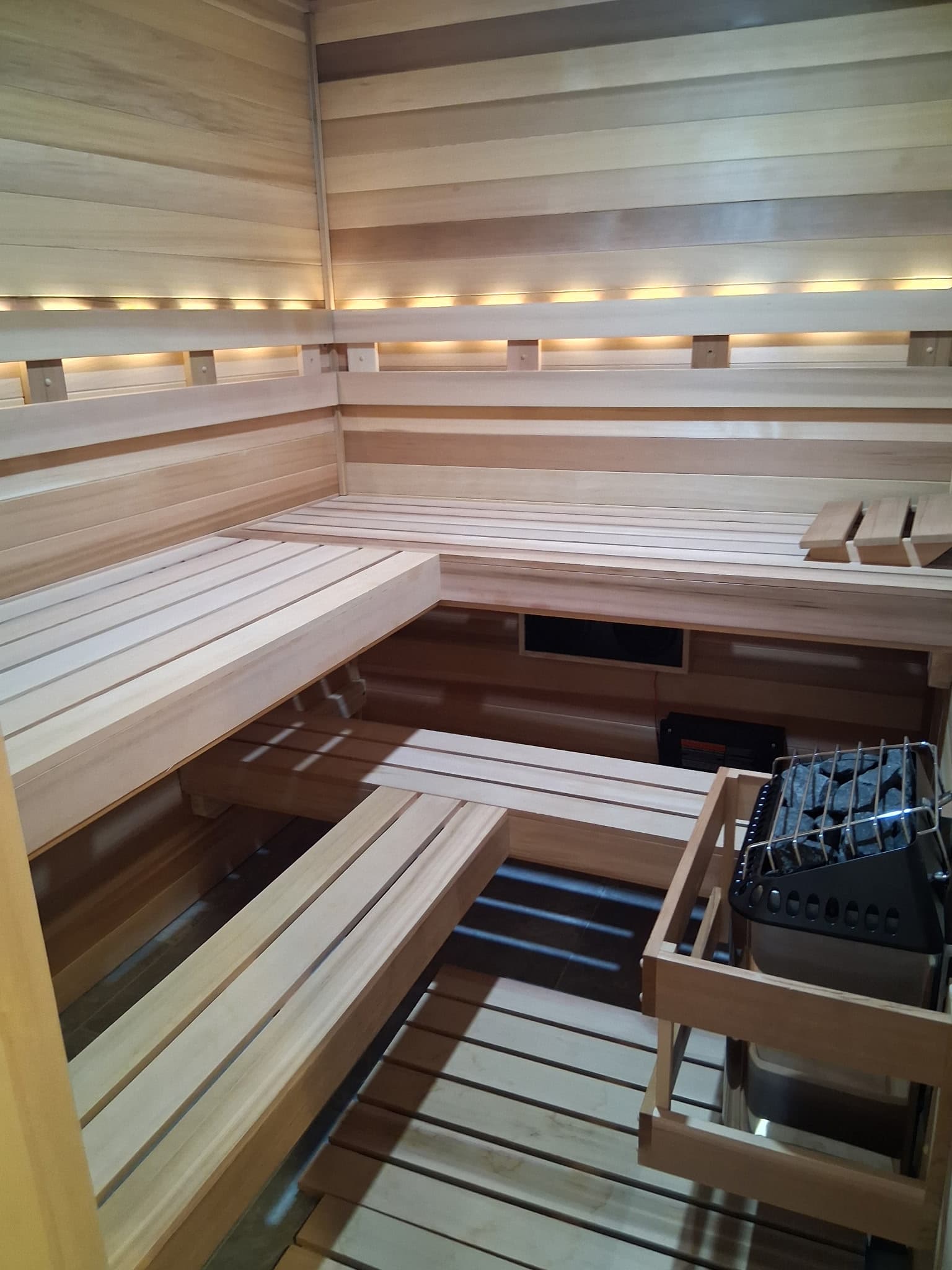 Finished custom indoor sauna with pale wood benches, heater, and layered bench heights.