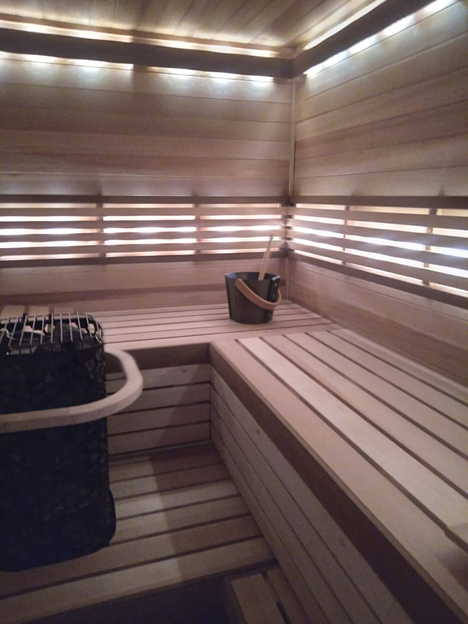 Finished sauna corner with upper bench lighting and sauna bucket.