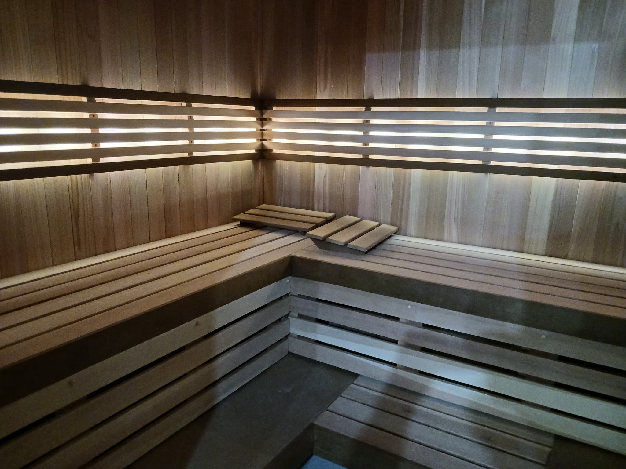 Finished sauna room with broad benches, horizontal backrests, and linear light.