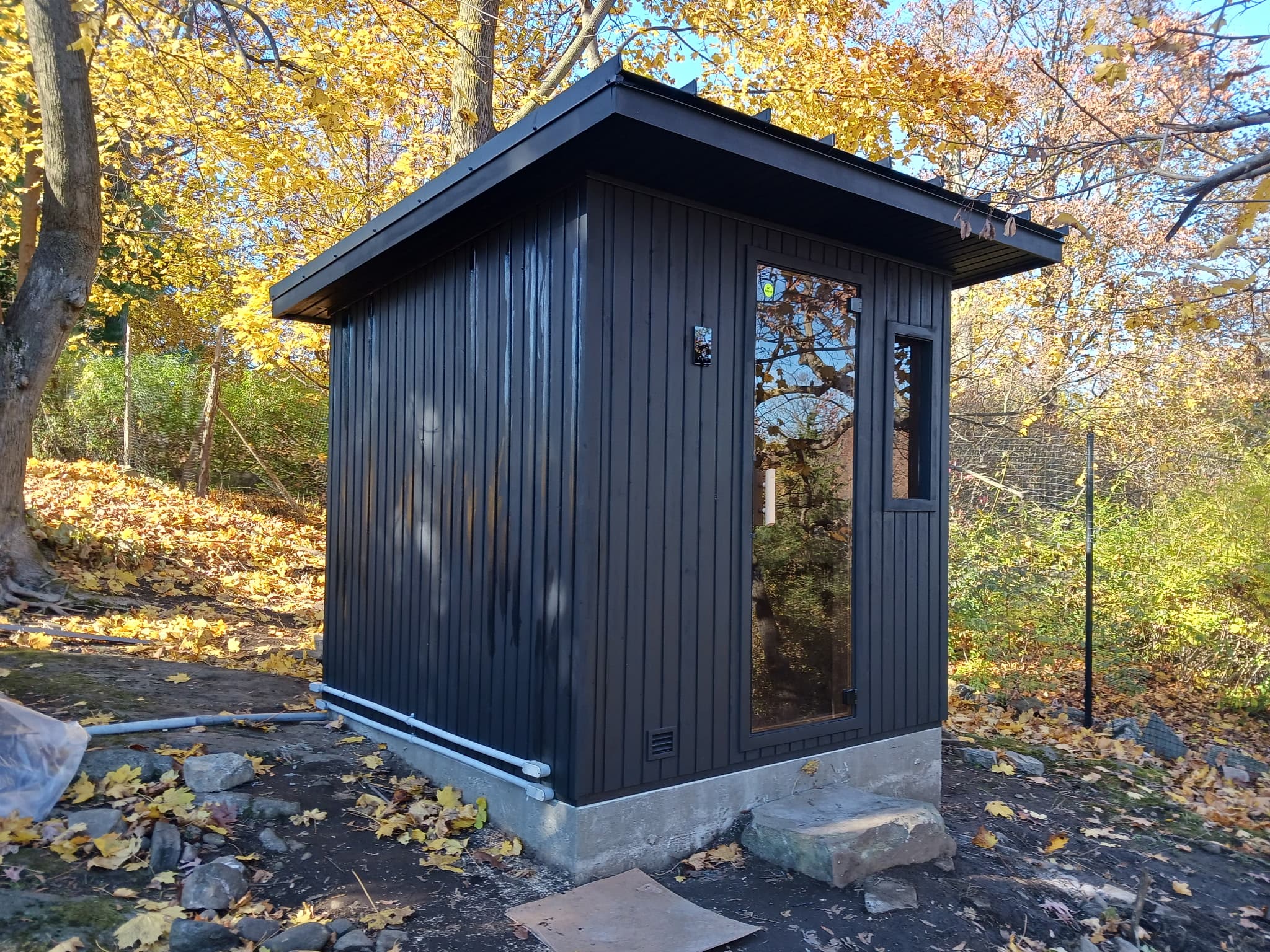 Dark exterior outdoor sauna cabin in a wooded landscape.