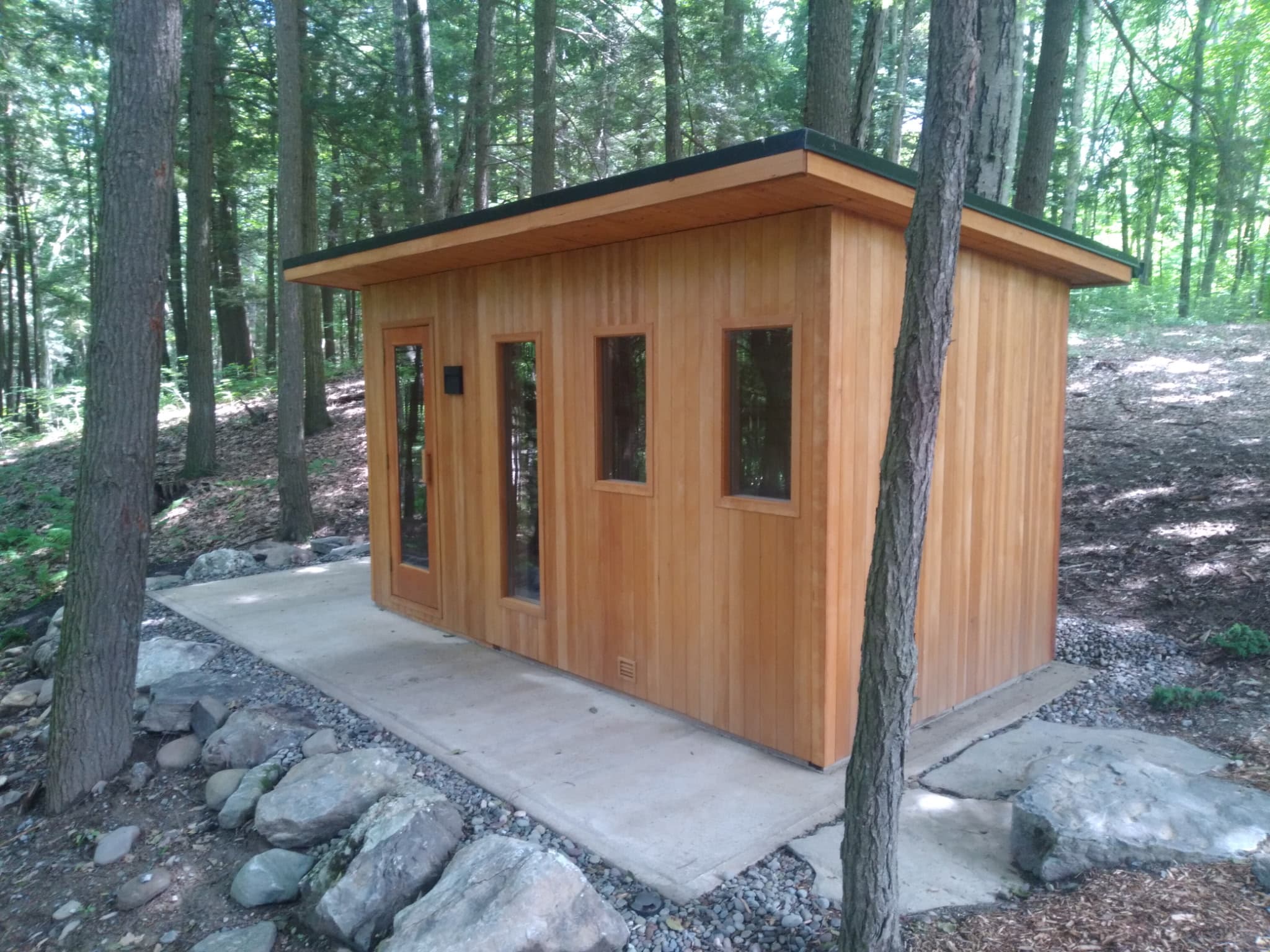Completed cedar outdoor sauna in a wooded setting.