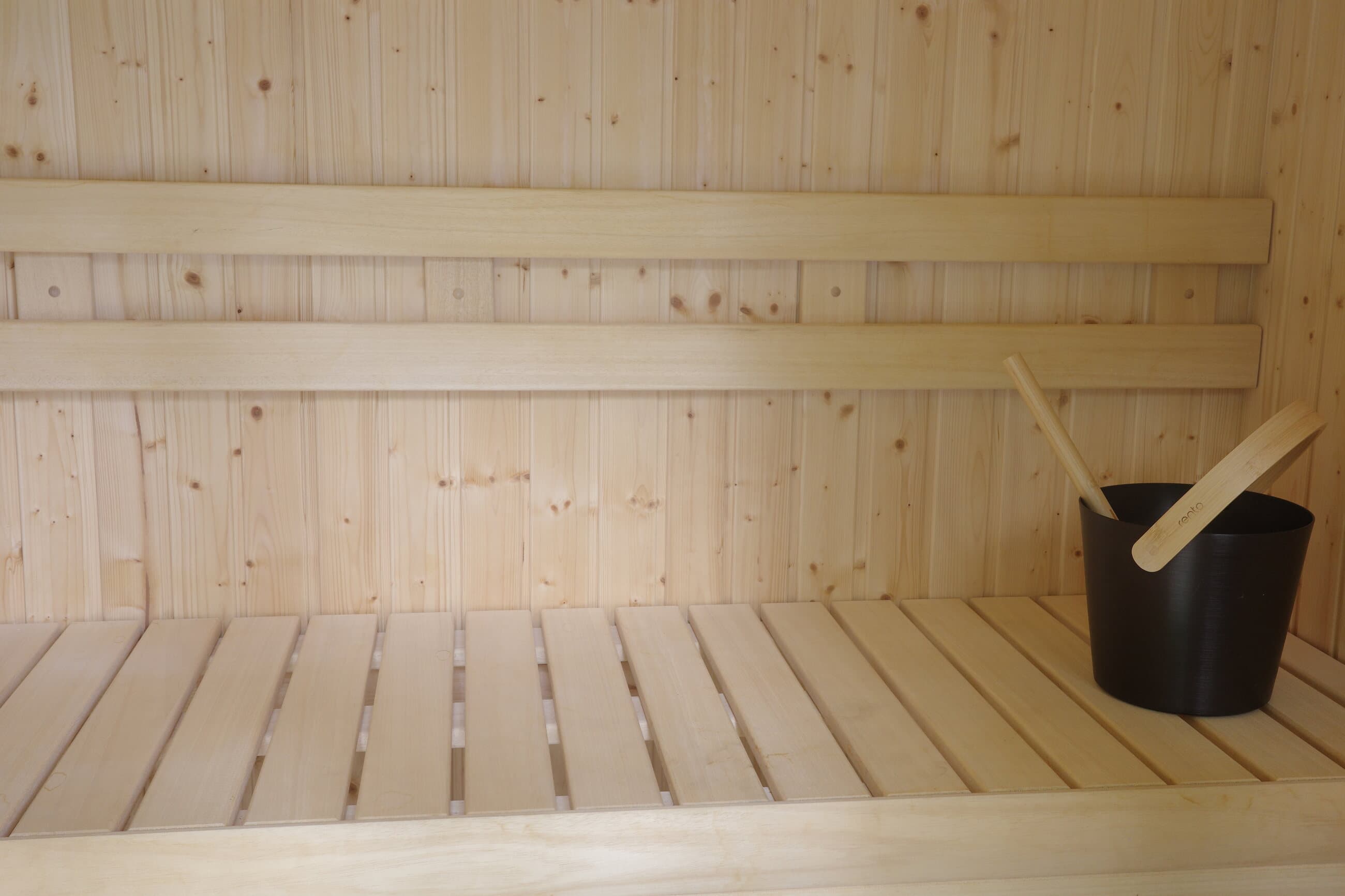 Finished pale wood sauna bench with black sauna bucket and ladle.