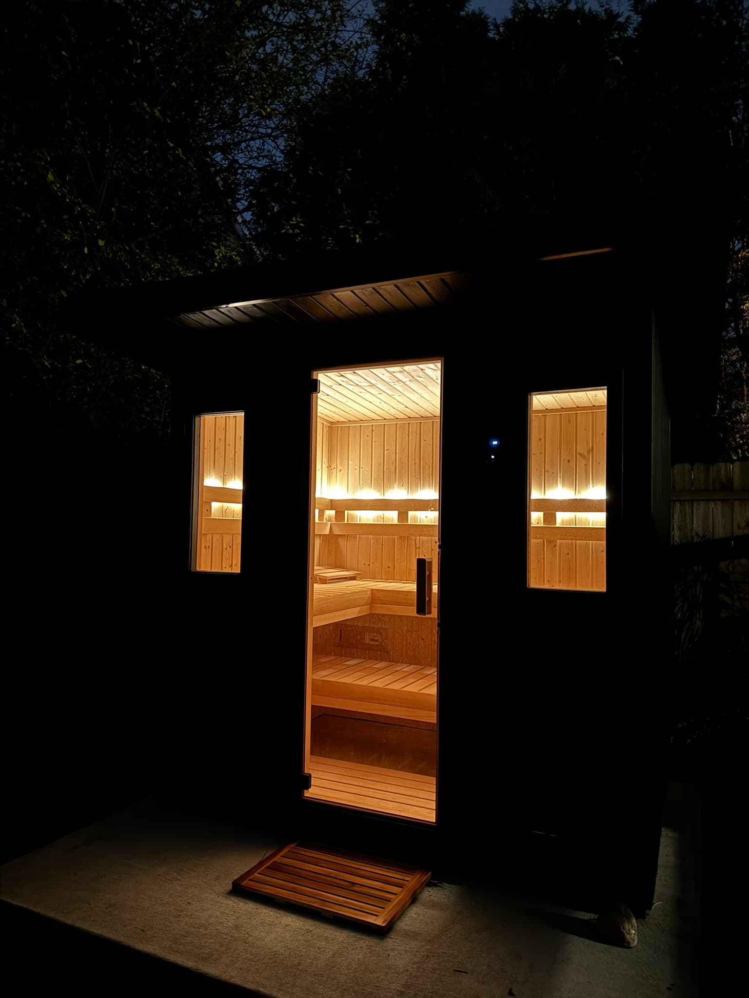 Outdoor sauna entry at night with the lit wood interior visible through the open door.