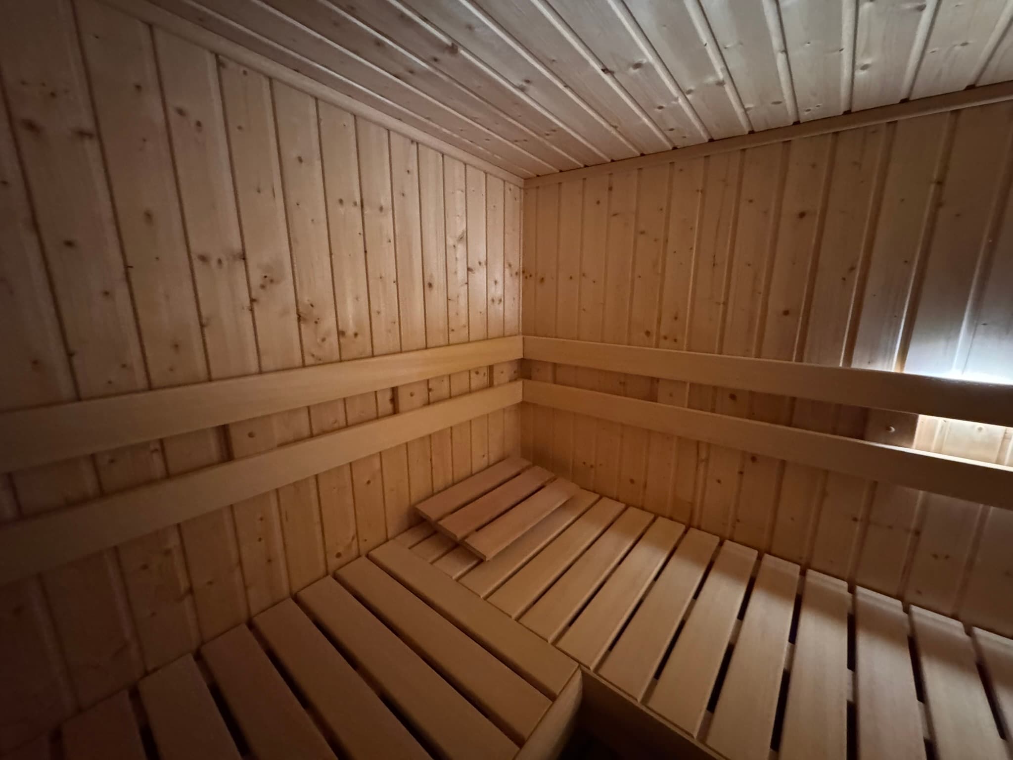 Finished sauna interior with wraparound benches, vertical wood walls, and concealed backrest lighting.