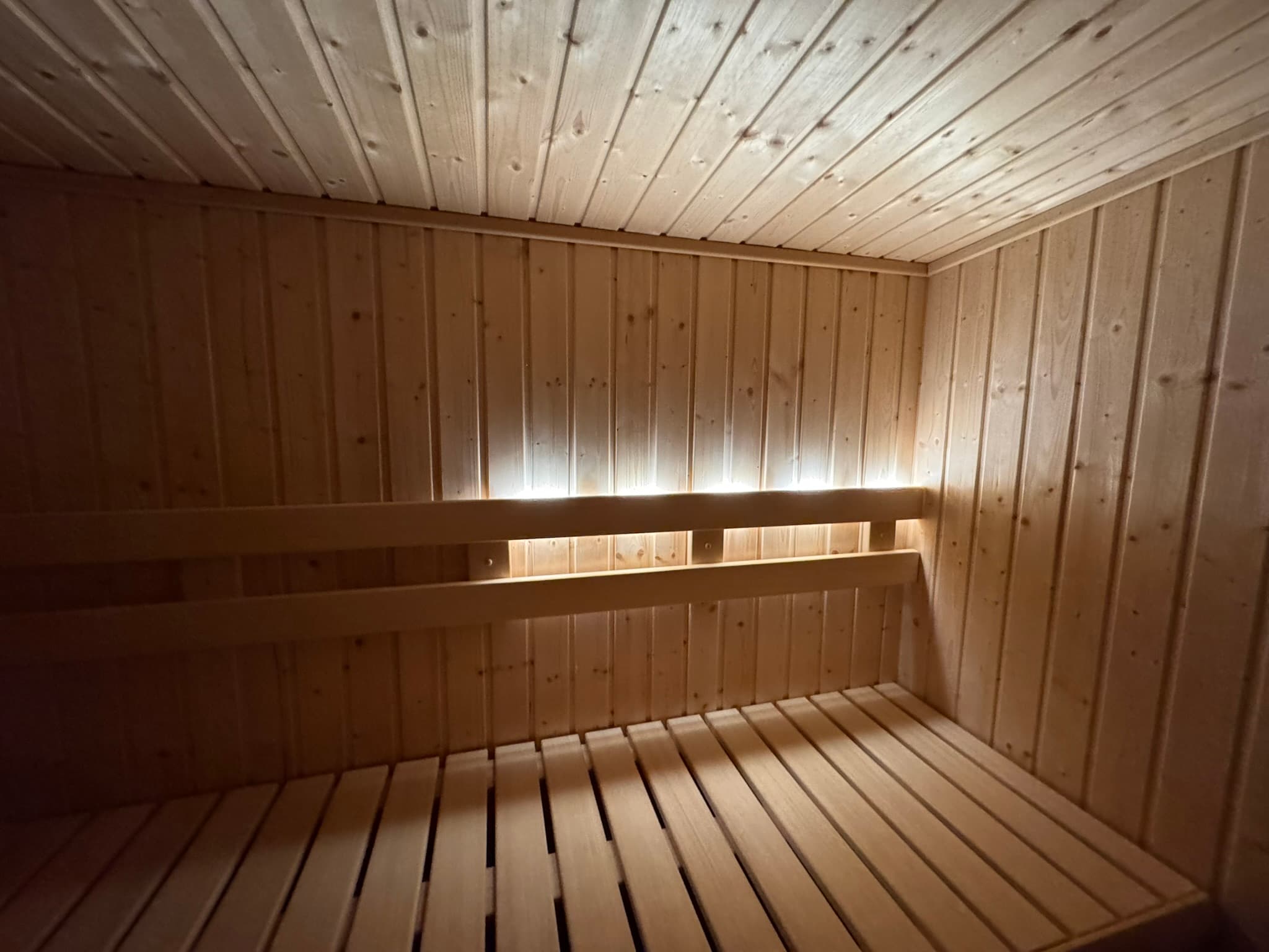 Finished sauna interior with broad bench seating, vertical wood walls, and backrest lighting.